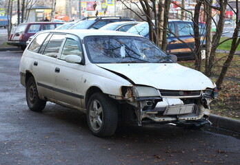 Naklejka premium An old white wrecked passenger car is parked on the street, ulitsa Kollontai, Saint Petersburg, Russia, November 2021