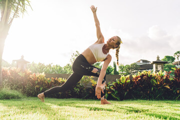 Fit woman in Side Angle pose on tropical lawn
