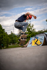 Junge in Jeans und T-Shirt und mit Helm macht Skateboardtrick Ollie mit Skateboard im Skatepark © Arthur Braunstein