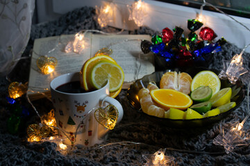 Cozy still life on the windowsill, with an open book, sweets, citrus notes and a garland in the form of asterisks - clothespins. The still life is located on a knitted scarf