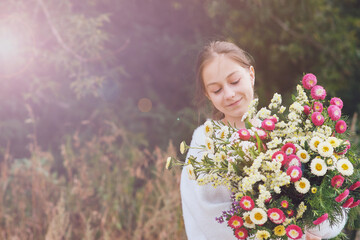 A young girl holds in her hands a large beautiful bouquet of autumn flowers and admires them