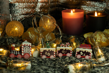 Christmas still life with a gingerbread train, a garland in the form of jars with a Christmas tree and snow. The still life is located on a knitted scarf, which gives the photo an atmosphere