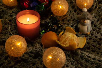 Fototapeta na wymiar Christmas still life with sweets, tangerines, candles, a garland in the form of balls woven from threads and a penguin figurine. The still life is located on a knitted scarf