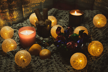 Christmas still life with sweets, two candles, a garland in the form of balls woven from threads. The still life is located on a knitted scarf, which gives the photo an atmosphere and comfort. 