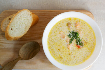Salmon and cream fish soup in a white bowl on a wooden cutting board with a few slices of bread. Lohikeitto is a traditional Finnish and Karelian soup. Top view.