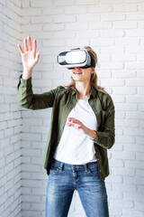 Amazed woman in VR glasses standing on white brick wall background