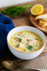 Salmon and cream fish soup in a white bowl with a spoon and a few slices of bread. Lohikeitto is a traditional Finnish and Karelian soup. Rustic style. Horisontal orientation.