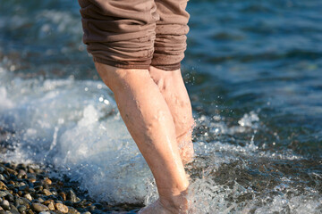 The legs of an elderly woman with altered varicose veins on the background of the sea in autumn....