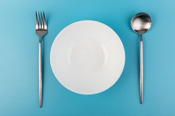 Empty plate with fork and spoon on blue background. Flat lay Dishes for breakfast, lunch or dinner Mock up
