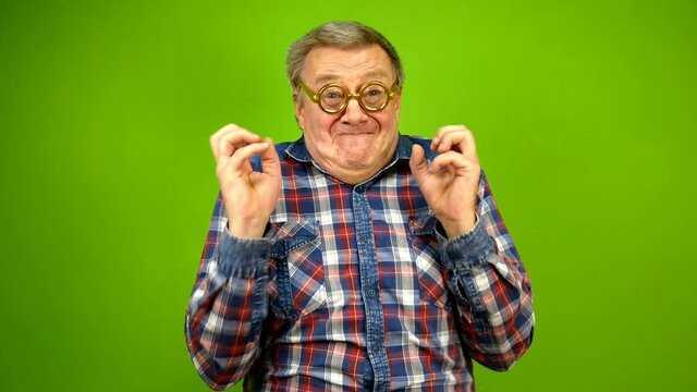 Mature adult strange man in stupid glasses is emotionally happy about something, claps his hands and shakes his hands with delight. Green screen.