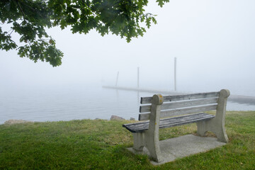 Empty bench sits on the shoreline of a small beach enveloped in fog