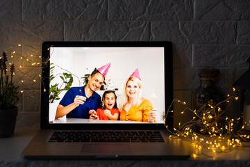 Happy parents hugging cute small kid daughter holding present giving Christmas gift to web camera during virtual family social meeting on video conference call party at home, laptop webcam view.