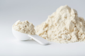 A mountain of soy protein isolate in powder with a measuring spoon on a white background.
