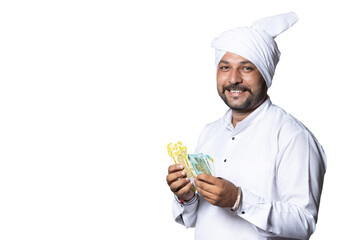 Portrait of young happy Indian rural mustache man wearing kurta and turban standing over isolated white background holding Indian currency notes, village male with beard smiling with cash money.