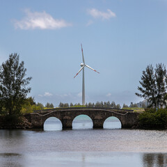 A single wind turbine stands behind the beautiful stone arched bridge. A wind power station rises...