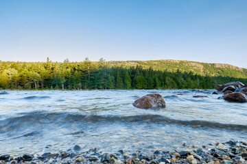 Granite boulders and smaller broken up and smoothed rocks line the shoreline of Jordan Pond in...