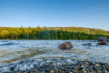 Granite boulders and smaller broken up and smoothed rocks line the shoreline of Jordan Pond in...