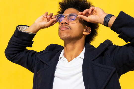 Stylish Black Man Adjusting Glasses Against Yellow Wall