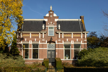 Large Dutch brick exterior facade of stately home surrounded by autumn colors against a clear blue sky. Real estate and housing market concept in The Netherlands.