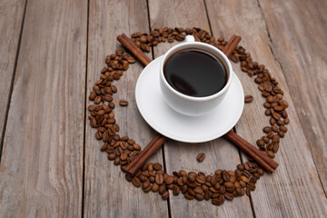 Top view of cup of coffee with cinnamon surrounded coffee beans on wooden table
