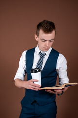 A young man in a business suit with a notebook and a mug of coffee in his hands. Guy on a brown background.