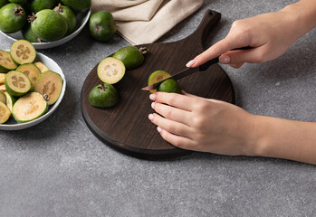 girl cuts feijoa dark wooden board . Concept for preparing products for smoothies and juices