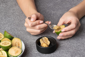 female hands hold half of feijoa and spoon out pulp of the berry with spoon to make an antioxidant green smoothie and sweet jam.