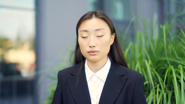 Asian female office worker relax, meditates outdoor sitting on a bench on urban background a city park resting a break Business woman employee in formal suit, eyes closed. Silence, tranquility calm