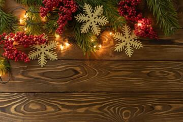 Christmas background. Nobilis fir branches, twigs with red berries, toy golden snowflakes on brown wooden planks. Copy space, flat lay, top view. Holiday, Xmas, New Year concept. Mockup