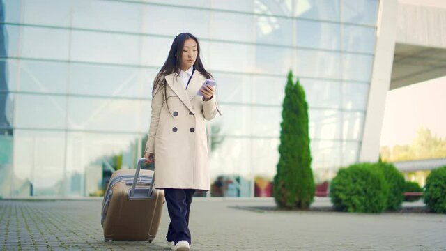 Asian female tourist businesswoman walks with suitcase from terminal airport background a modern urban train station a city street. Using holding mobile phone in his hands. Woman business trip