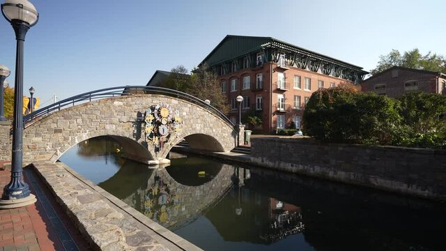 Day time autumn view of bridge in popular city park, Carroll Creek Park in historic district of Frederick with shops and building on sides of the canal. People walking.