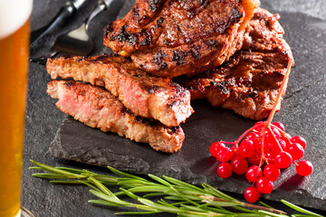 Delicious hearty food. Grilled juicy cuts of meat, hot steak with rosemary, red berries on a slate stone board. Top view.