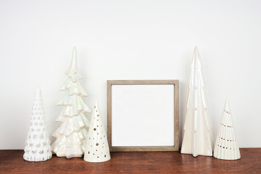 Christmas mock up with wood frame and shiny glass tree decor. Square frame on a wooden shelf against a white wall. Copy space.