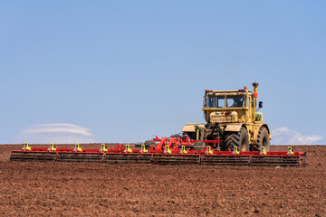 Obraz premium Tractor with a trailed combined tillage unit on arable land. Copy space.