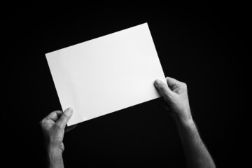 Hands holding blank sheet of paper against black background.
