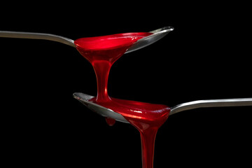 Fruit red jam dripping from spoon on black background