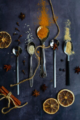 Vertical composition. Fragrant spices on spoons on a dark background. Cinnamon, anise, ginger, cloves. View from above