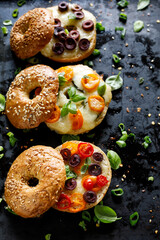 Grilled bagel sandwich  with with mix vegetables, mozzarella cheese and herbs on a dark background,  focus on the sandwich with cherry tomatoes and olives, close up view.