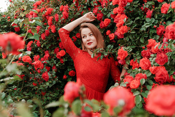 Portrait of a beautiful blonde in a red dress in a garden with red roses