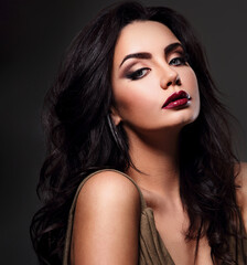 Fototapeta premium Beautiful bright makeup woman with long black curly hair style, burgundy lipstick with vamp look on dark grey background. Closeup