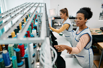 African American seamstress works at embroidery machine in textile factory.
