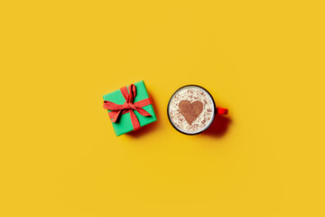 Holiday gift and cup of coffee with heart shape on yellow background.