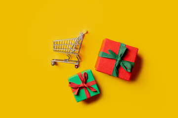 Two holiday gift boxes and supermarket cart on yellow background.