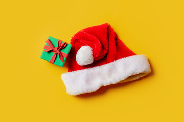 holiday gift box and Christmas Santa Claus hat on yellow background.