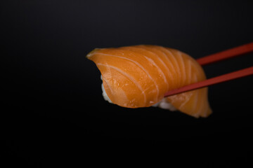 Red Chopstick keeping a piece of Salmon Nigiri Sushi on Black Background