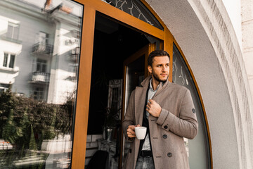 Fototapeta na wymiar Handsome man with cup of coffee posing in coat in cafe. Male lifestyle.