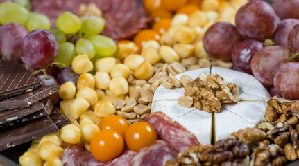 Appetizer for guests. A plate with cheese, salami, nuts, grapes and snacks on a black iron plate. Antipasto. Italian cuisine.