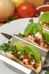 Closeup of three delicious gourmet chicken tacos on a silver tray with vegetables and cilantro and salsa.