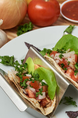 Closeup of three delicious gourmet chicken tacos on a silver tray with vegetables and cilantro and salsa.