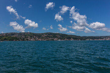 Fototapeta premium A beautiful scenic view to the green hills and houses over the blue Bosphorus under the beautiful blue sky with white cotton clouds on a sunny day.